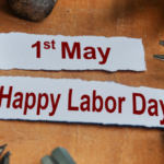 Close-up of a workbench with tools scattered around paper labels reading “1st May” and “Happy Labor Day.”
